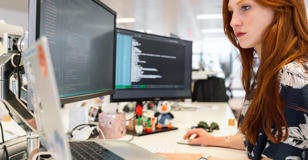 a focused female software engineer coding on dual monitors in a modern office