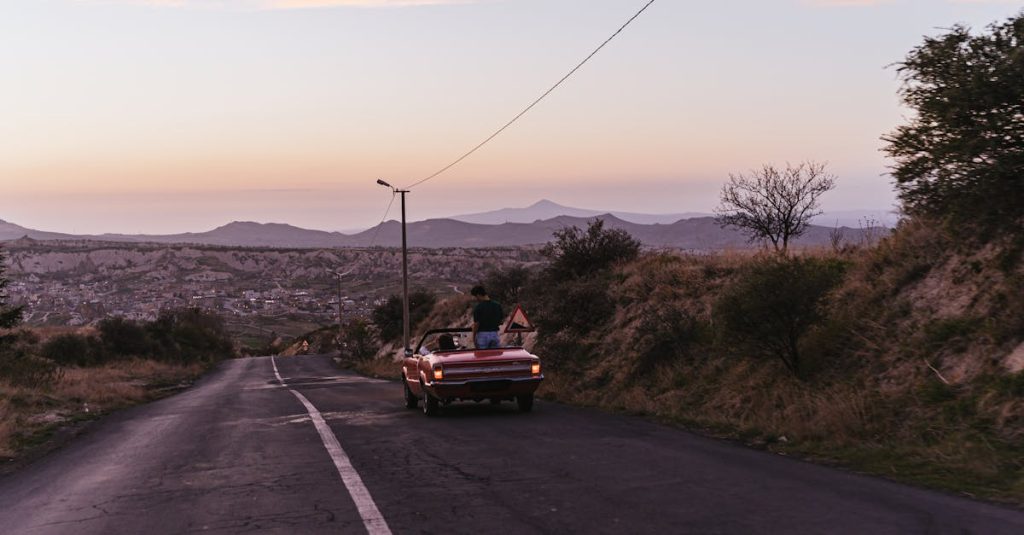 red convertible with two people driving on a scenic mountain road at sunset
